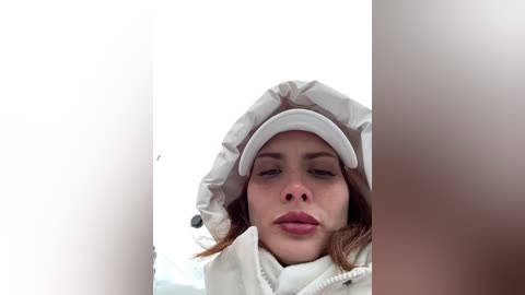 Media: Video of a young woman with light skin and long brown hair, wearing a white puffer jacket and a white cap, against a stark white background, giving a close-up, introspective look.