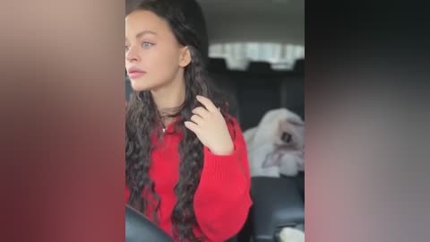 Media: Video of a young woman with long, dark hair, wearing a red sweater, sitting in a car with her hand on her neck, blurry background.