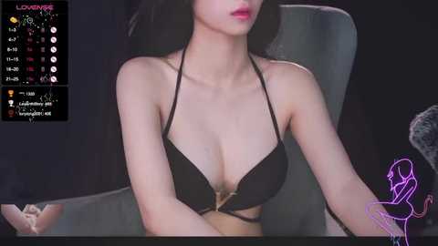 Media: Video of an East Asian woman with fair skin, dark hair, wearing a black bikini top, sitting in a chair. Background includes a digital calendar and a purple graphic of a woman.