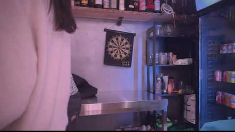 Media: Video of a dimly lit, cluttered basement room with a dartboard, shelves of bottles, and a person in a white shirt standing to the left.