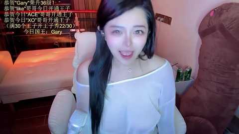 Media: A video of a young Asian woman with long black hair, wearing a white off-shoulder top, smiling in a cozy bedroom. Text overlay in Chinese and English.