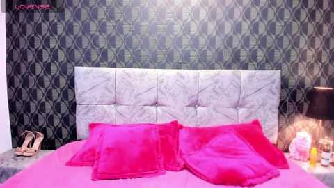 Media: Video of a modern bedroom with a plush pink bed, matching pink pillows, and a tufted white headboard. Dark, patterned wallpaper contrasts with a sleek black nightstand and lamp.