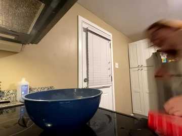 Media: Video of a kitchen with beige walls, a blue bowl on a black stove, a man in motion with a red mug, white cabinets, and a stainless steel range hood.