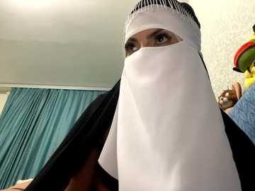 Media: A video of a person wearing a white veil over their face, with dark hair partially visible, standing in a room with teal curtains and colorful toys.