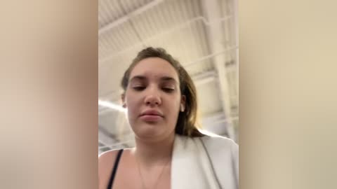 Media: Video of a young woman with light skin, brown hair, wearing a white robe, standing in a gym with white walls and ceiling.