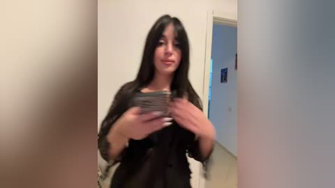 Media: A video of a young woman with long, dark hair, wearing a black dress, dancing with a smartphone in a beige room.