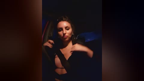 Media: Video of a woman with medium skin tone, dark hair, and wearing a black strapless dress, sitting in a dimly lit car, her right arm resting on the window frame, creating a dramatic, moody ambiance.