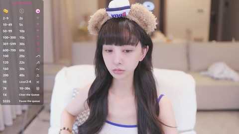 Media: Video of a young East Asian woman with long black hair, wearing a white sailor hat with bear ears and a sailor dress, sitting on a white couch in a modern living room.