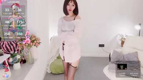 Media: Video of a slender Asian woman with shoulder-length brown hair in a white off-shoulder dress, posing in a modern, minimalist bedroom with white walls, pink flowers, and a green chair.