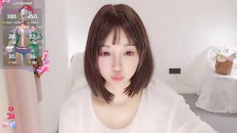 Media: A video of a young Asian woman with a short bob haircut, wearing a white top, in a minimalistic, white room. The image overlays a character from a video game.