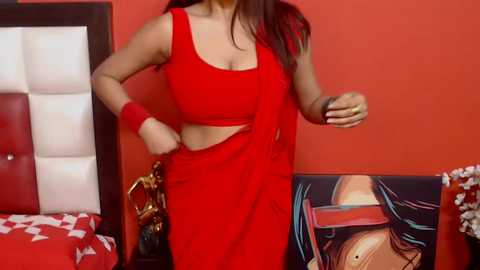 Media: Video of a woman in a red saree and red wristbands, standing in a room with red walls, white tufted headboard, and a colorful abstract painting.