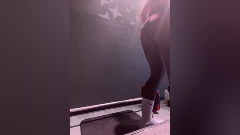 Media: A video of a person with long hair in black leggings and white socks jogging on a treadmill, with a dimly lit background featuring a starry pattern on the wall.