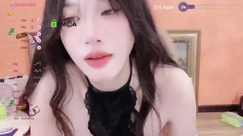 Media: Video of a young Asian woman with pale skin, long black hair, and a black lace choker, in a pink room with a framed picture, green wall decor, and a bed in the background.