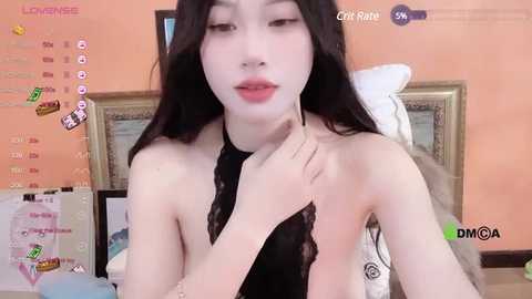 Media: A video of a young East Asian woman with long black hair, light skin, and a slender physique, wearing a black lace top, sitting in a bedroom. The background features a pink wall, a bed, and various virtual stickers.