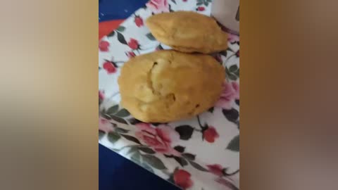 Media: A video shows two golden-brown, slightly cracked, round cookies on a floral-patterned napkin with red, pink, and green flowers, placed on a blue surface.