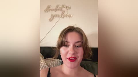 Media: Video of a fair-skinned woman with brown hair, wearing red lipstick, smiling, with \"believe you love\" wall text above.