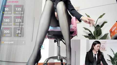 Media: Video of an East Asian woman in a black suit and sheer black tights, seated on a pink office chair, with a virtual reality display overlaying temperature data on the left.