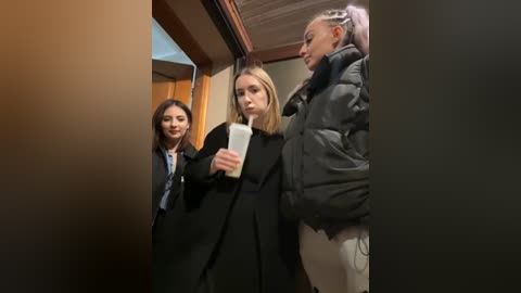 Media: Video of three women in a dimly lit corridor; one sips a drink, another holds a bag, and the third wears a puffer jacket.