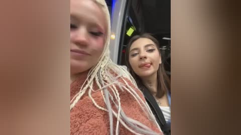 Media: Video of two young women: a blonde with dreadlocks and a tan skin tone, and a brunette with straight hair, both smiling. They are inside a car, with a blurred background.