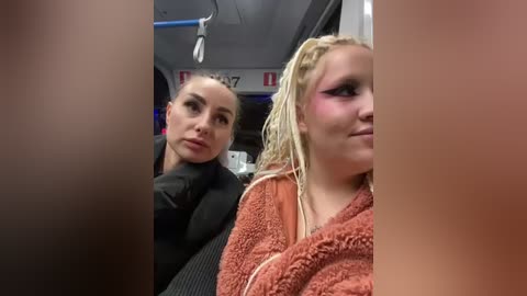 Media: Video of two women in a car: a blonde woman with light makeup, wearing a black jacket, sits next to a young blonde woman with dreadlocks and purple eyeshadow, wrapped in a brown blanket.