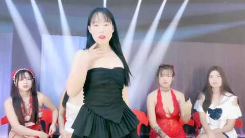 Media: Video of four Asian women in revealing outfits, including a black strapless dress, red bikini, white top, and red halter dress, standing in a spotlighted room with bright lights.