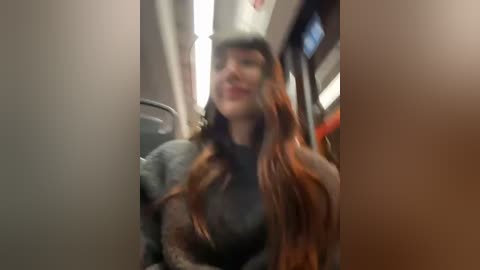 Media: Video of a woman with long, wavy red hair, wearing a dark jacket, sitting on a bus. Her face is blurred, creating a sense of motion. The background shows bus interior details.