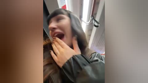 Media: Video of a young woman with light skin and dark hair, wearing a brown leather jacket, smiling and holding a man's hand in a subway train.