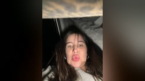 Media: A video of a young woman with long brown hair and fair skin, making a kissy face, peering through a car sunroof, with a cloudy sky above.