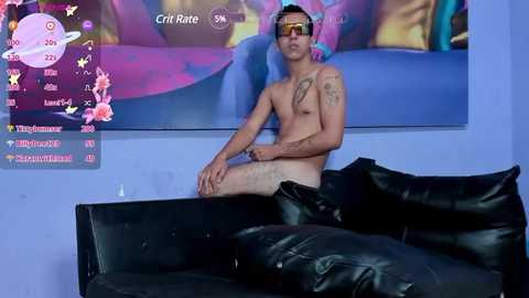 Media: Video of a shirtless, tattooed, fair-skinned man with sunglasses, sitting on a black leather couch, surrounded by colorful, abstract digital art on a purple wall.