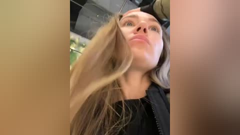 Media: Video of a Caucasian woman with long, blonde hair, wearing a black jacket, looking up into a microscope, taken from a low angle, with a blurred background.