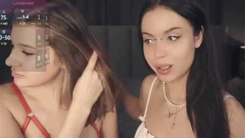 Media: Video of two young women; one adjusting another's hair, both with fair skin, long dark hair, and wearing casual outfits.