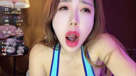 Media: Video of a young East Asian woman with long, straight brown hair and fair skin, wearing a blue and white halter top, her mouth open in a suggestive expression.