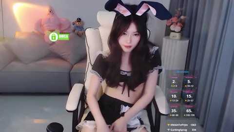 Media: Video of a young Asian woman in a bunny costume, sitting on a white chair, with a video game overlay in the background.