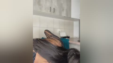 Media: A video of a person wearing black lace stockings and a teal dress, lying on a bed with white walls and a minimalist bathroom in the background.