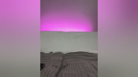 Media: A video depicting a bed with a white pillow, grey blanket, and a soft pink glow from a light source above, creating a serene, minimalist bedroom ambiance.