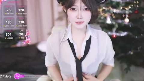 Media: Video of a young, slender East Asian woman with fair skin, wearing a white blouse, black tie, and black hair in a bun, standing in front of a Christmas tree.