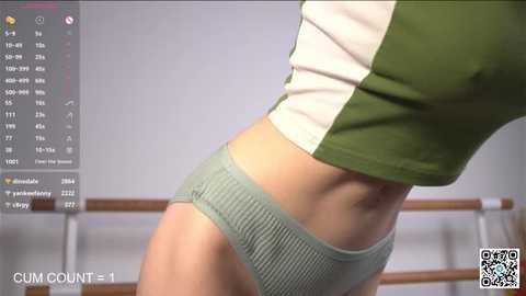 Media: A close-up video of a slender, light-skinned woman in green and white striped crop top and matching ribbed panties, standing in a ballet studio with mirrored walls and wooden bars in the background.