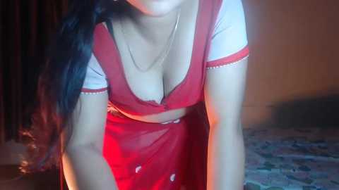 Media: Video of a woman with long, dark hair, wearing a low-cut red and white peasant blouse, revealing ample cleavage, leaning forward, indoors with dim lighting.