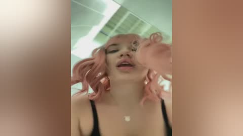 Media: A video of a young woman with pink wavy hair, wearing a black top, giving a blowjob to a penis. The setting appears to be an office with fluorescent lighting and ceiling tiles.