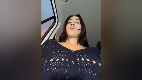 Media: A video of a young woman with long dark hair, fair skin, and a slender physique, wearing a black, lace-textured top. She is seated inside a car, with the window partially open.