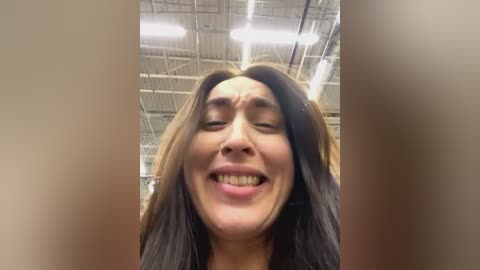 Media: A video of a joyful woman with long brown hair, closed eyes, and an open-mouthed smile, captured from a low angle in an industrial setting with exposed metal beams and lights.