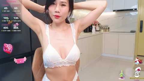 Media: Video of a young Asian woman with fair skin, black hair, wearing white lace lingerie, standing in a modern kitchen with white cabinets and stainless steel appliances.