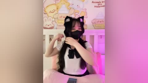 Media: Video of an Asian woman with long black hair, wearing a black cat hood and mask, adjusting a black bow tie, against a colorful, cartoon-themed wall.