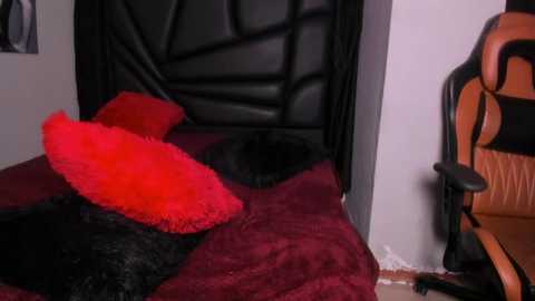 Media: A video of a cozy bedroom with a black leather headboard, red and black faux fur pillows, a black cat, and a gaming chair with orange accents.