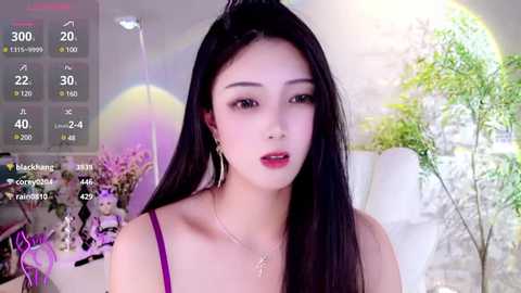 Media: Video of a young Asian woman with long black hair, fair skin, and bright red lipstick. She wears a purple spaghetti strap top and gold earrings. Background features a green plant and digital stats in the corner.