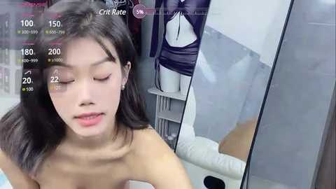 Media: A video of an Asian woman with straight black hair, wearing minimal makeup, and topless, standing in a clothing store near a mannequin dressed in a black leather jacket.