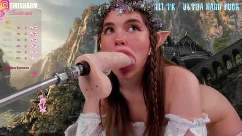 Media: Video of a young, fair-skinned woman with long brown hair, dressed as an elf, sucking on a large, realistic, flesh-colored dildo, set against a fantasy forest background.