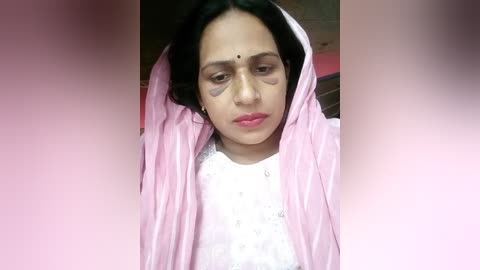 Media: Video of a young woman with a light brown complexion, wearing a pink shawl and a white embroidered blouse, looking sad with tear tracks on her face.