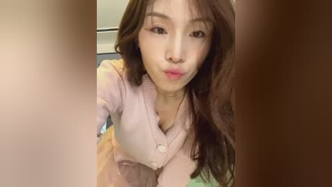 Media: Video of an Asian woman with long brown hair and fair skin, puckering her lips. She wears a pink cardigan and is indoors with blurred background.