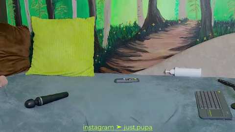 Media: A video of a cozy bedroom with a green forest mural, a yellow pillow, a grey keyboard, and a black phone on a blue duvet.